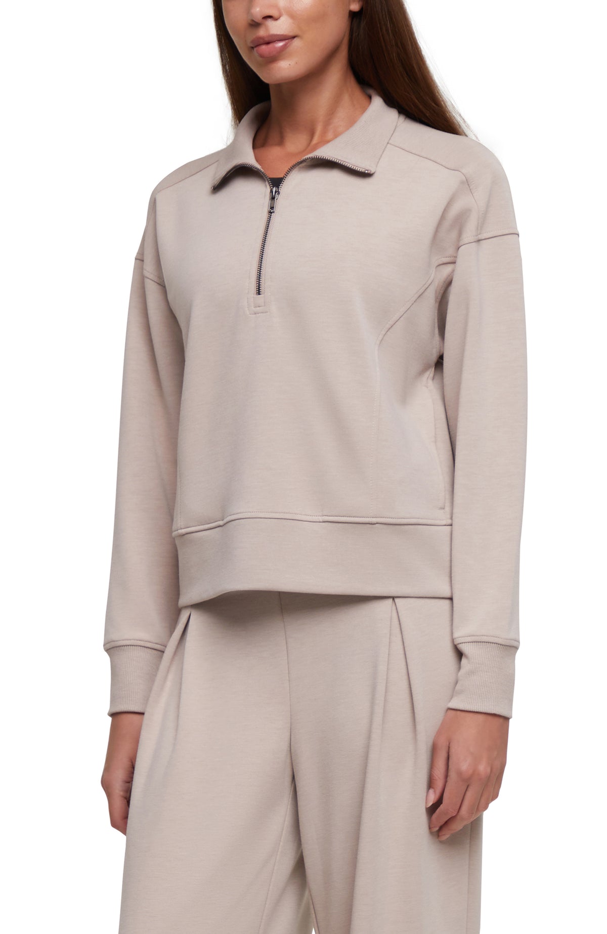 A woman wearing a light beige half-zip pullover sweatshirt with matching wide-leg sweatpants, shown from the neck down against a plain white background.