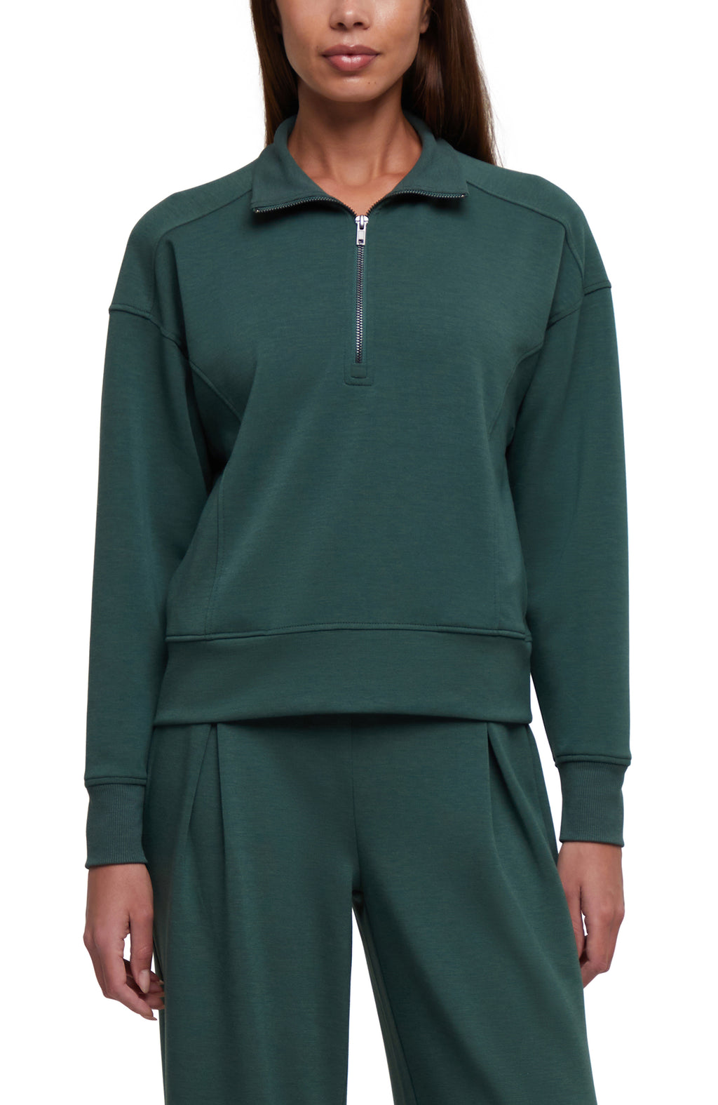 A woman wearing a dark green long-sleeve quarter-zip sweatshirt and matching sweatpants against a plain white background.