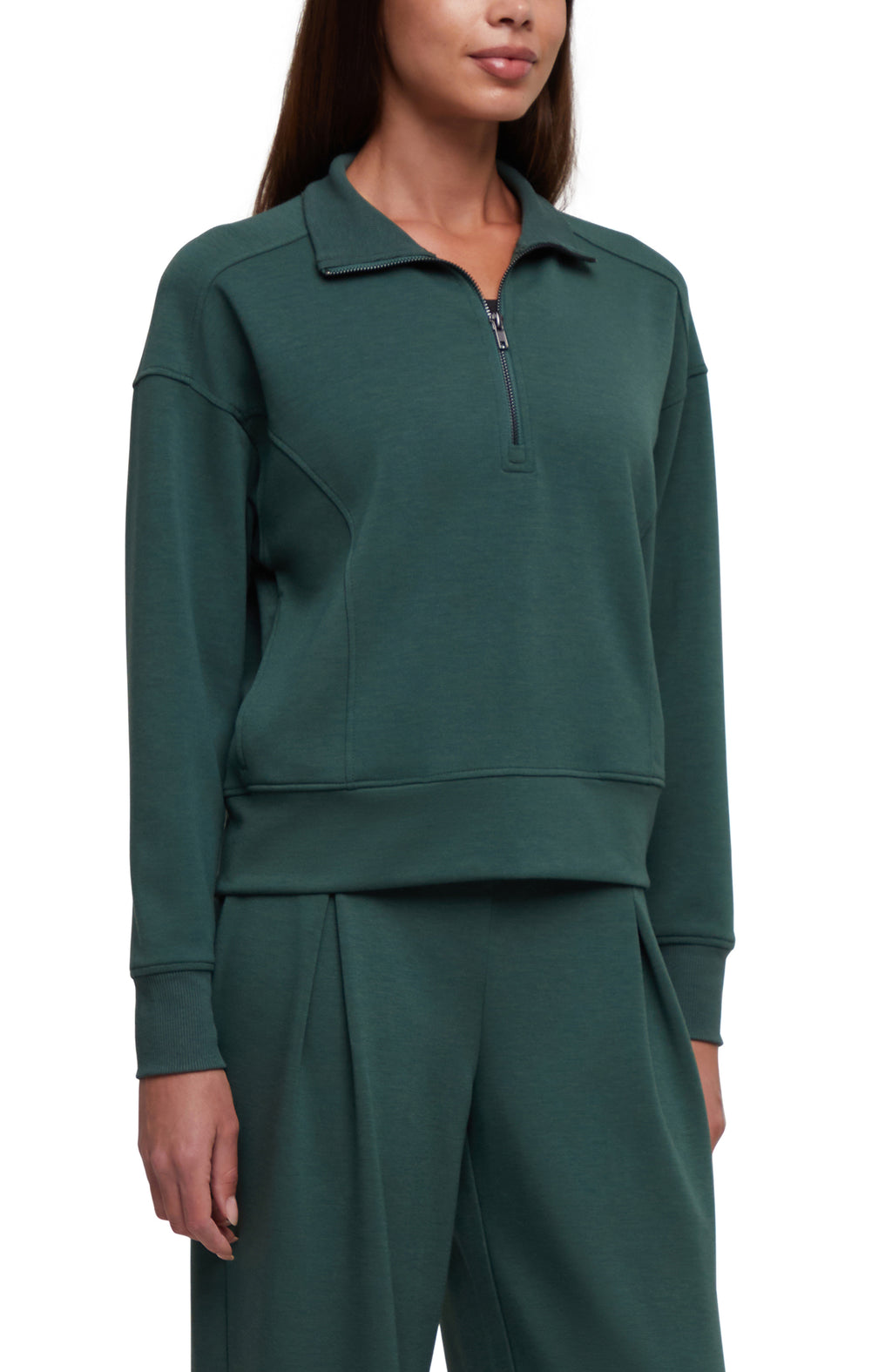 A woman wearing a dark green long-sleeve quarter-zip sweatshirt and matching dark green sweatpants, shown from the nose down against a plain white background.