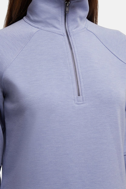 Close-up of a person wearing a light periwinkle blue quarter-zip pullover with a mock neck collar and silver zipper. 