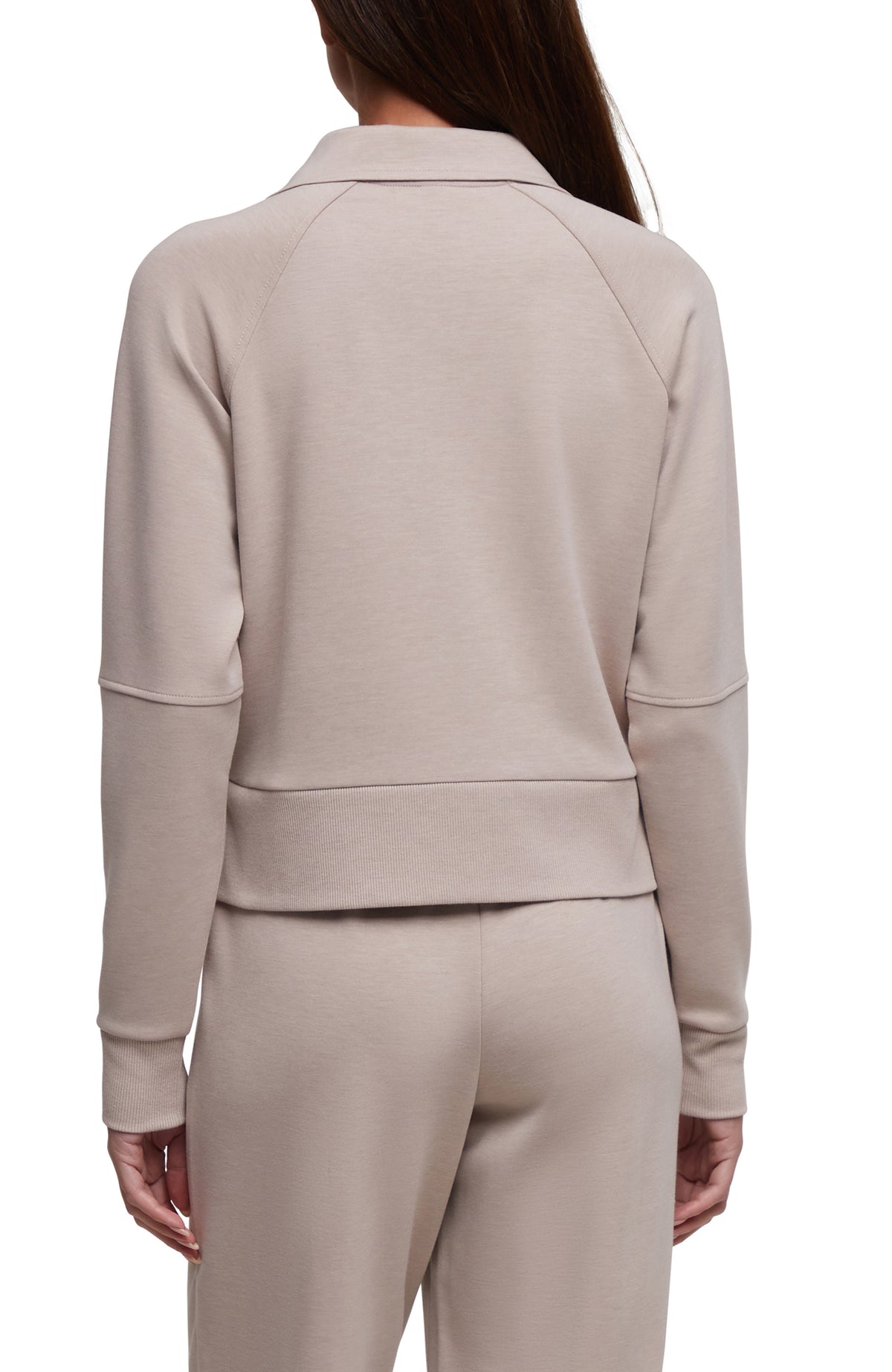 A model shown from the back wearing a light taupe-beige long-sleeve cropped quarter-zip sweatshirt and matching sweatpants against a plain white background. 