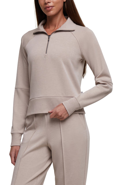 A woman wearing a light taupe-beige long-sleeve quarter-zip pullover and matching jogger pants against a plain white background. 