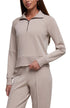 A woman wearing a light taupe-beige long-sleeve quarter-zip pullover and matching jogger pants against a plain white background. 