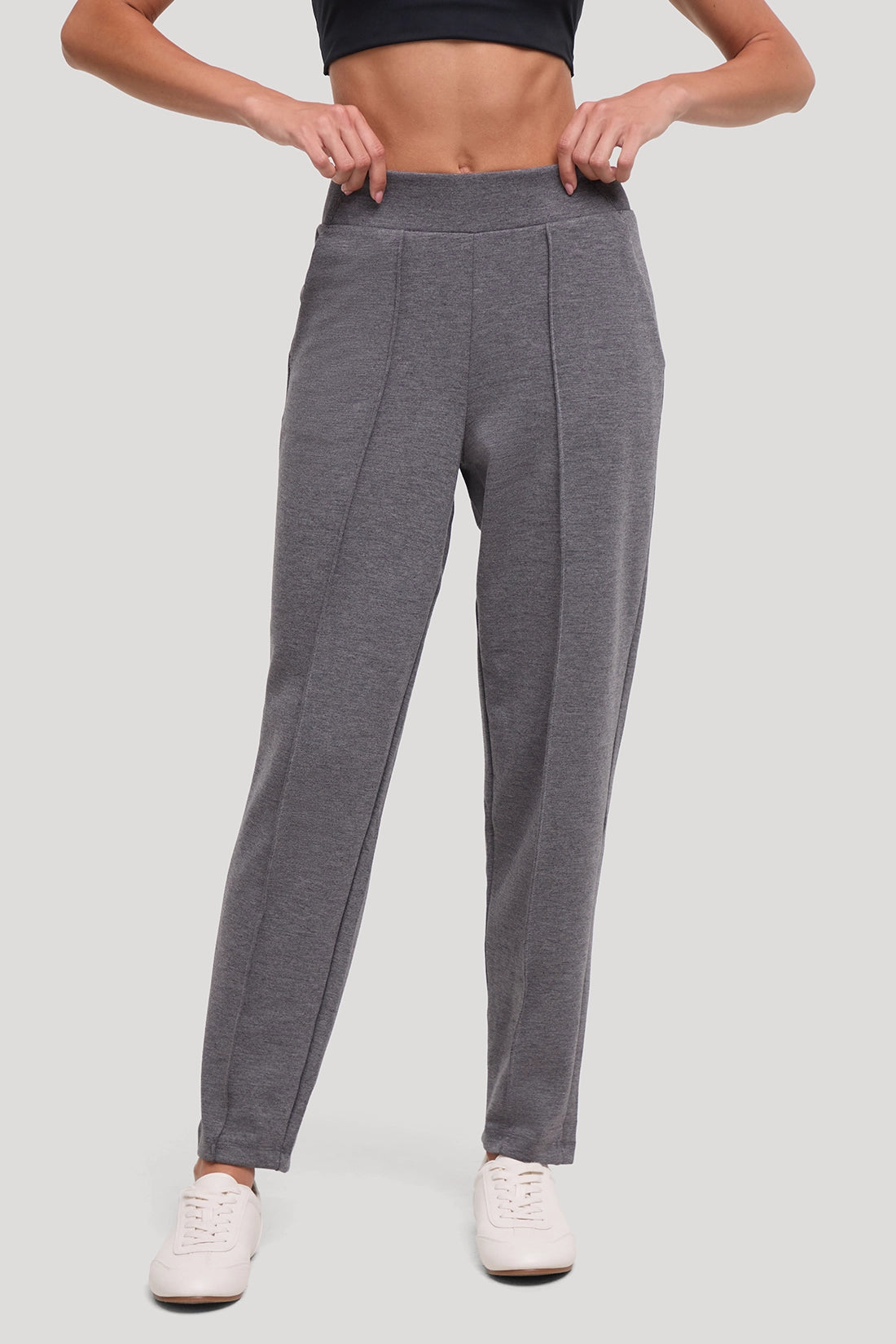 A person wearing heather gray athletic jogger-style pants with a wide elastic waistband and front seam detailing, paired with white sneakers against a light gray studio background. #color_heather-black