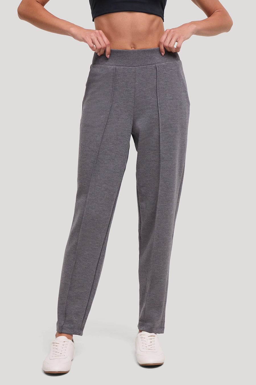 A person wearing heather gray athletic jogger-style pants with a wide elastic waistband and front seam detailing, paired with white sneakers against a light gray studio background. #color_heather-black
