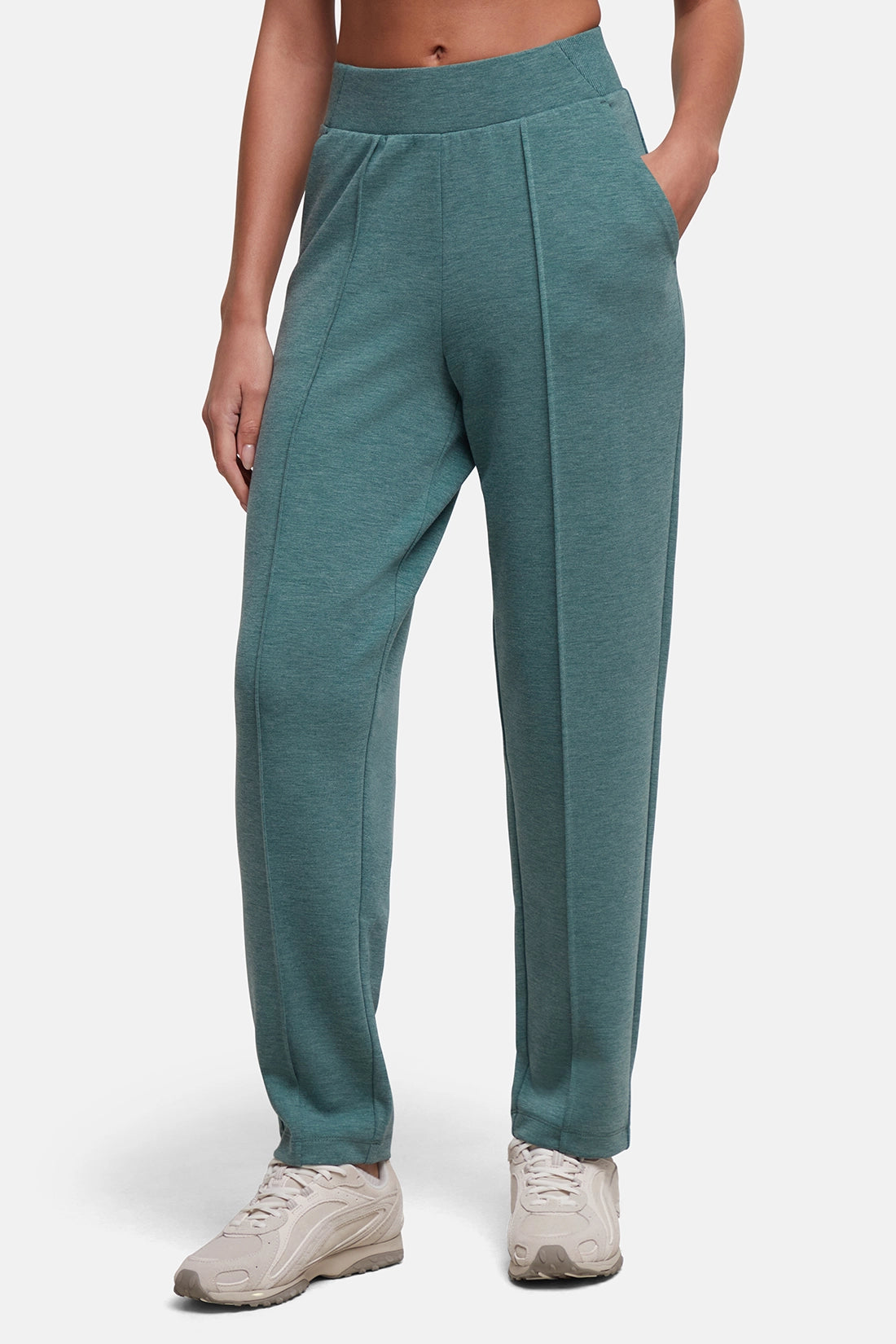 A woman modeling a pair of relaxed-fit heathered teal tapered leg with side pockets and a wide waistband, paired with light beige sneakers against a clean light gray studio background. #color_heather-botanical-garden
