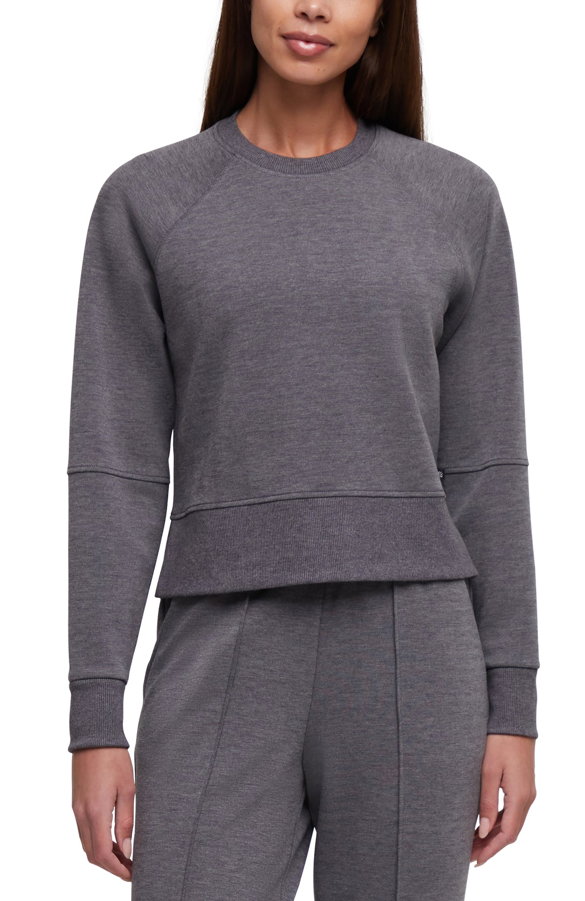 A woman wearing a dark gray heathered long-sleeve crewneck sweatshirt and matching gray heathered sweatpants, shown from the nose down against a plain white background. #color_heather-black
