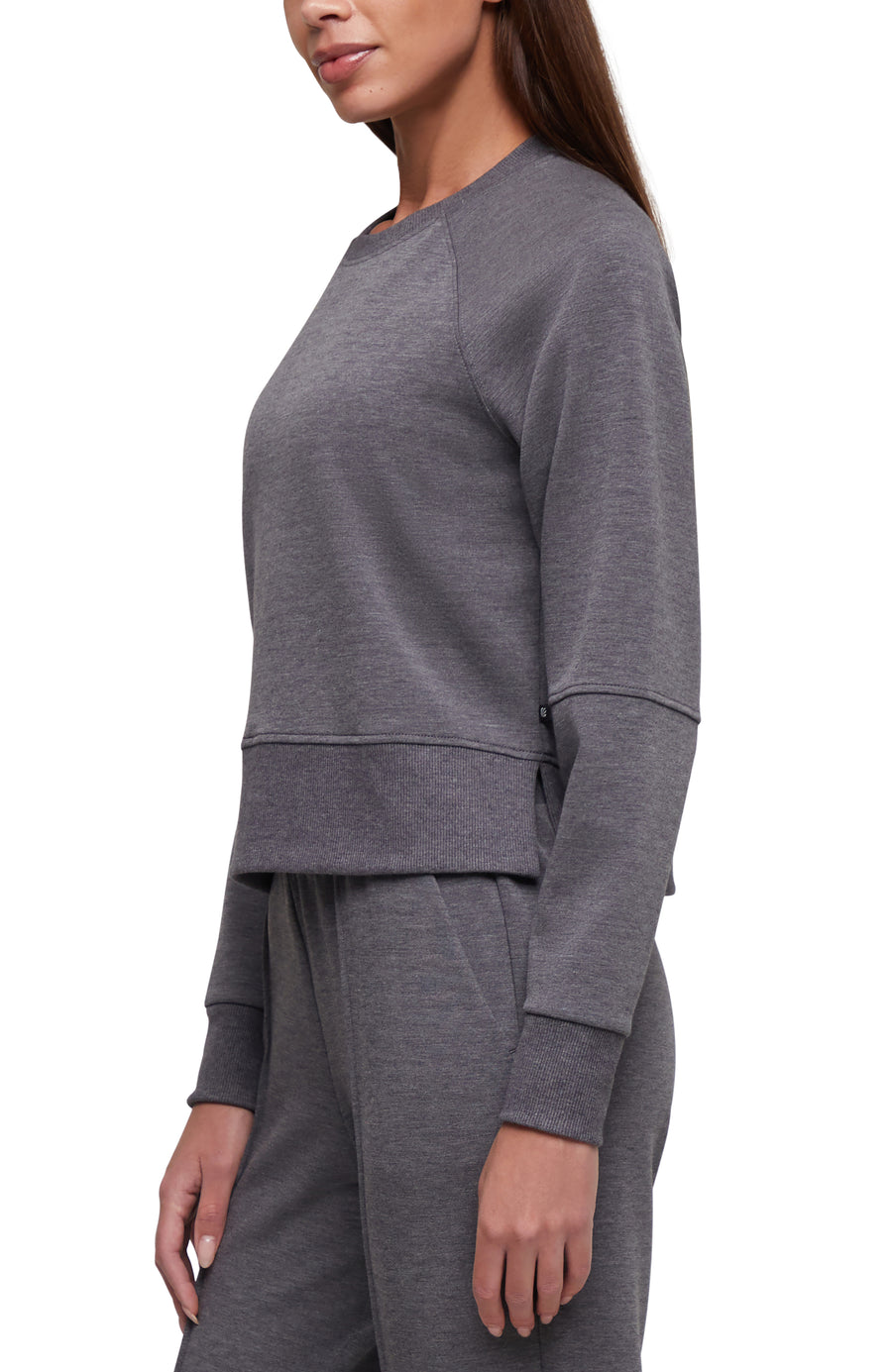 A woman wearing a heather gray long-sleeve cropped sweatshirt and matching jogger pants, shown in a side-profile studio shot against a white background. #color_heather-black