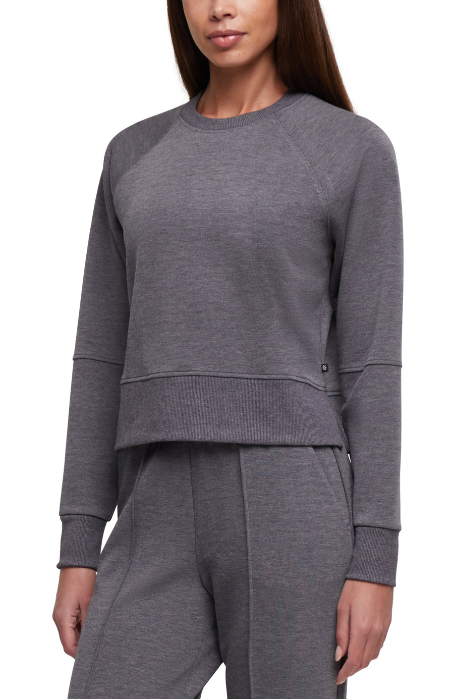 A woman wearing a dark gray heather cropped long-sleeve sweatshirt with ribbed cuffs and hem, paired with matching gray heather pants, shown against a plain white background. #color_heather-black