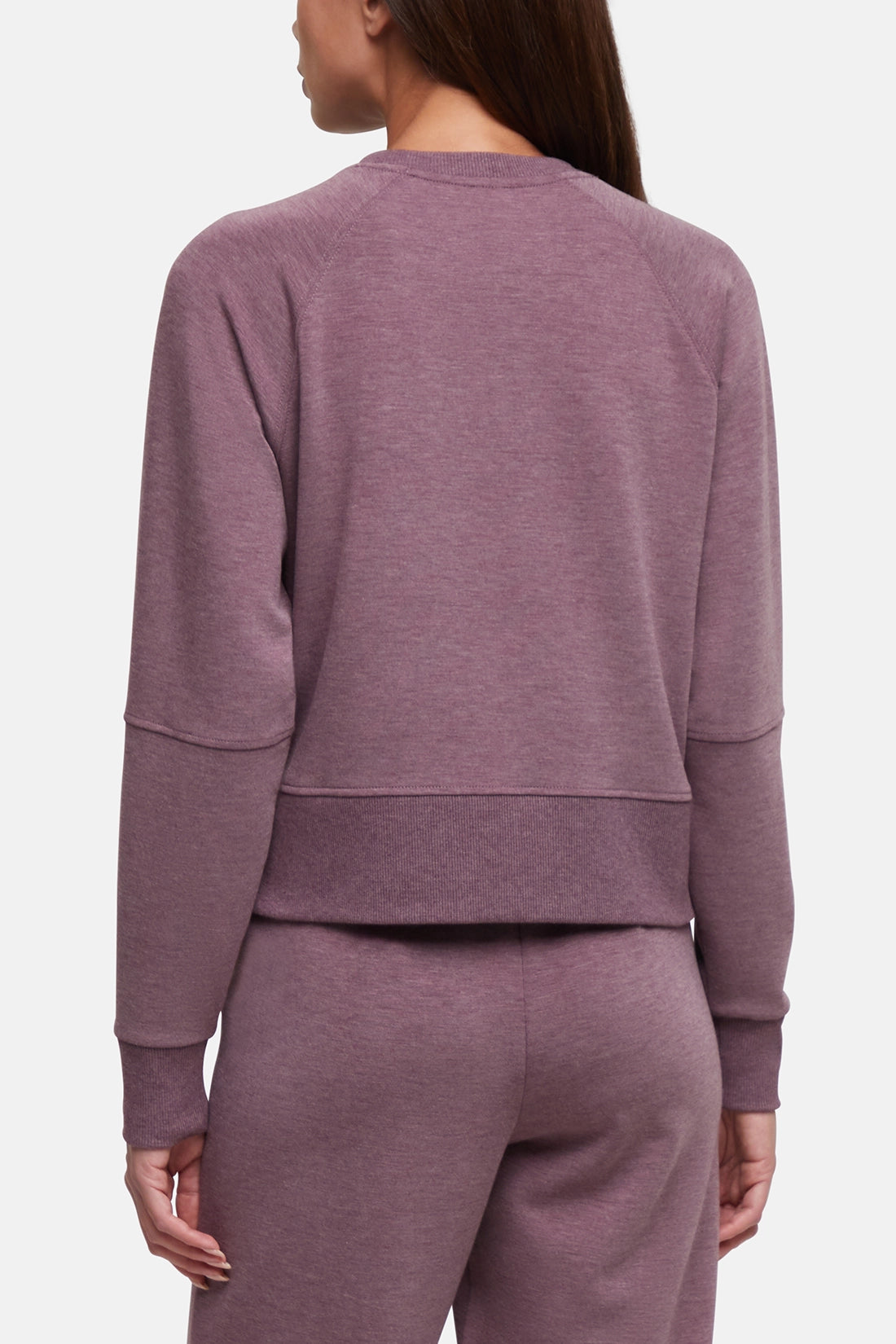 A woman shown from the back wearing a heathered dusty mauve crewneck sweatshirt and matching sweatpants against a light gray studio background. #color_heather-fig