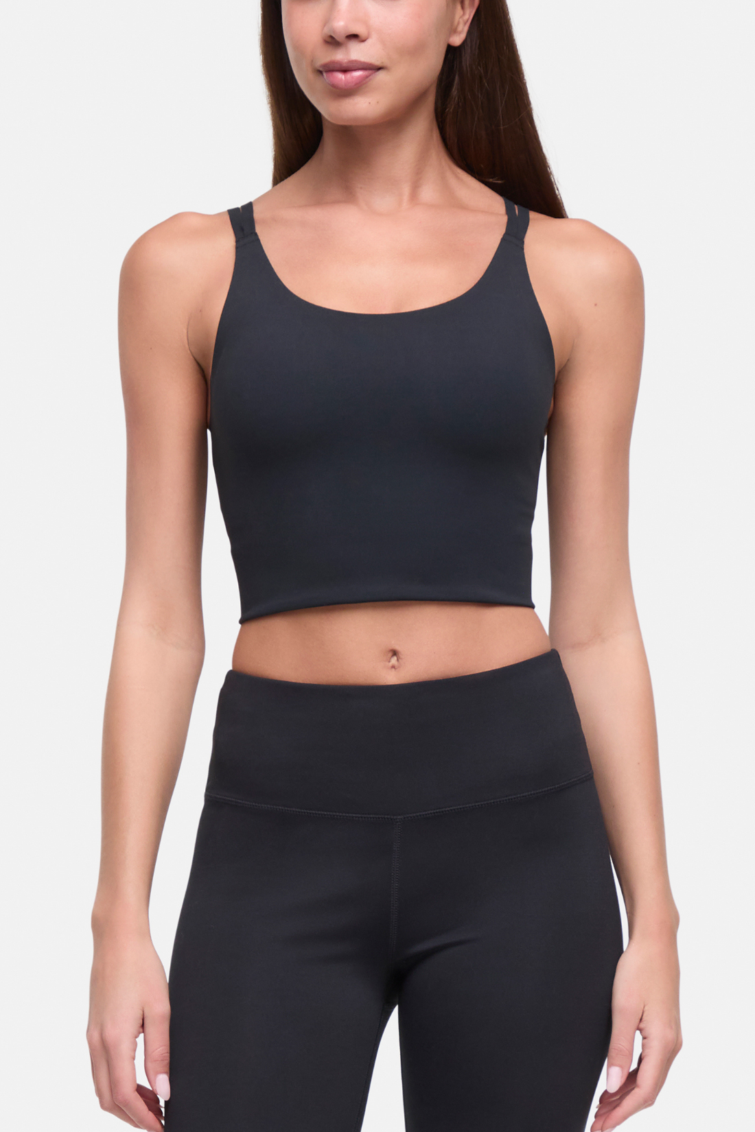 A woman modeling a dark charcoal gray athletic crop sports bra and matching high-waisted leggings against a light gray studio background. #color_black