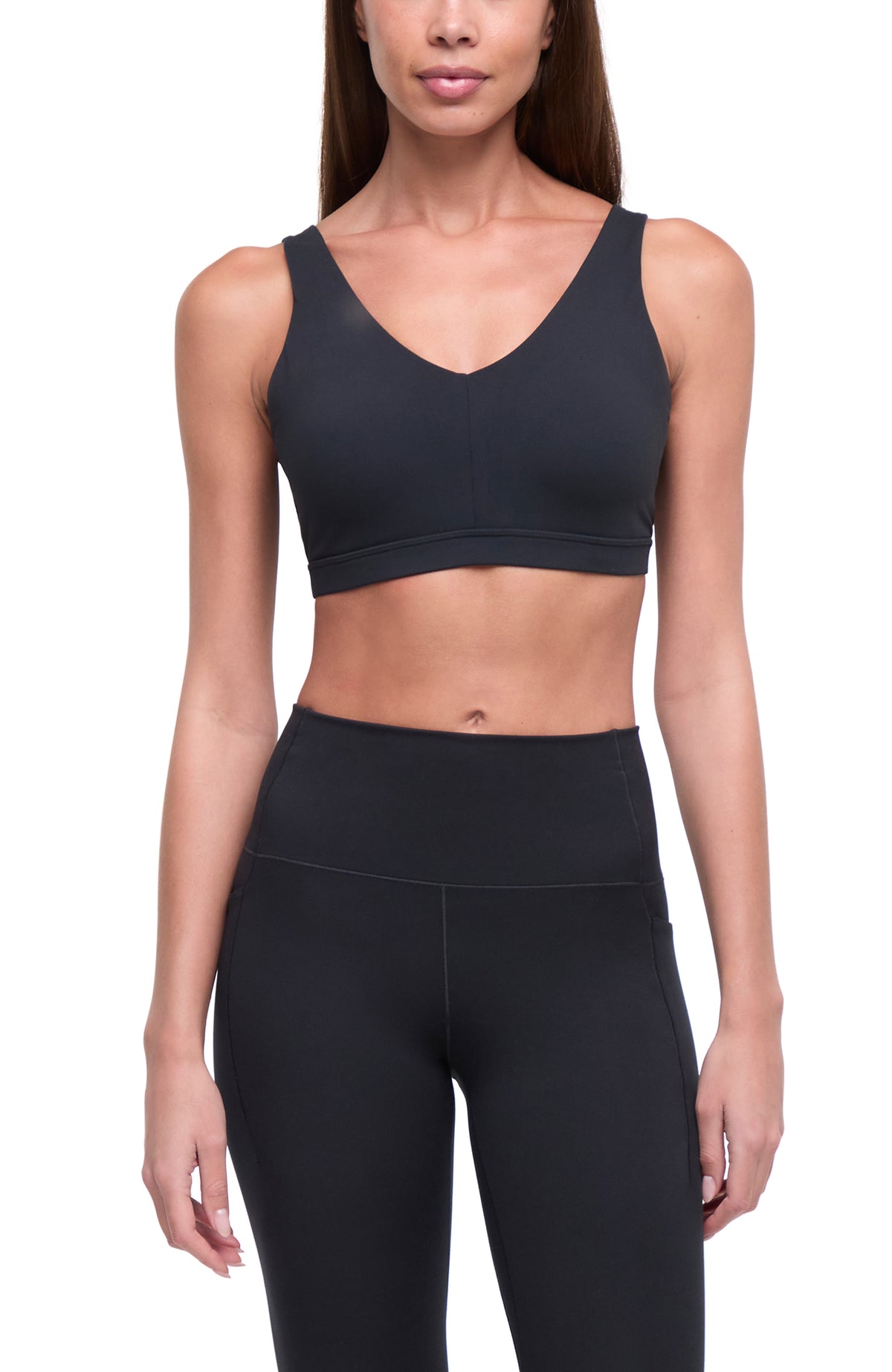 A woman modeling a black sports bra and matching high-waisted black leggings against a plain white background. #color_black