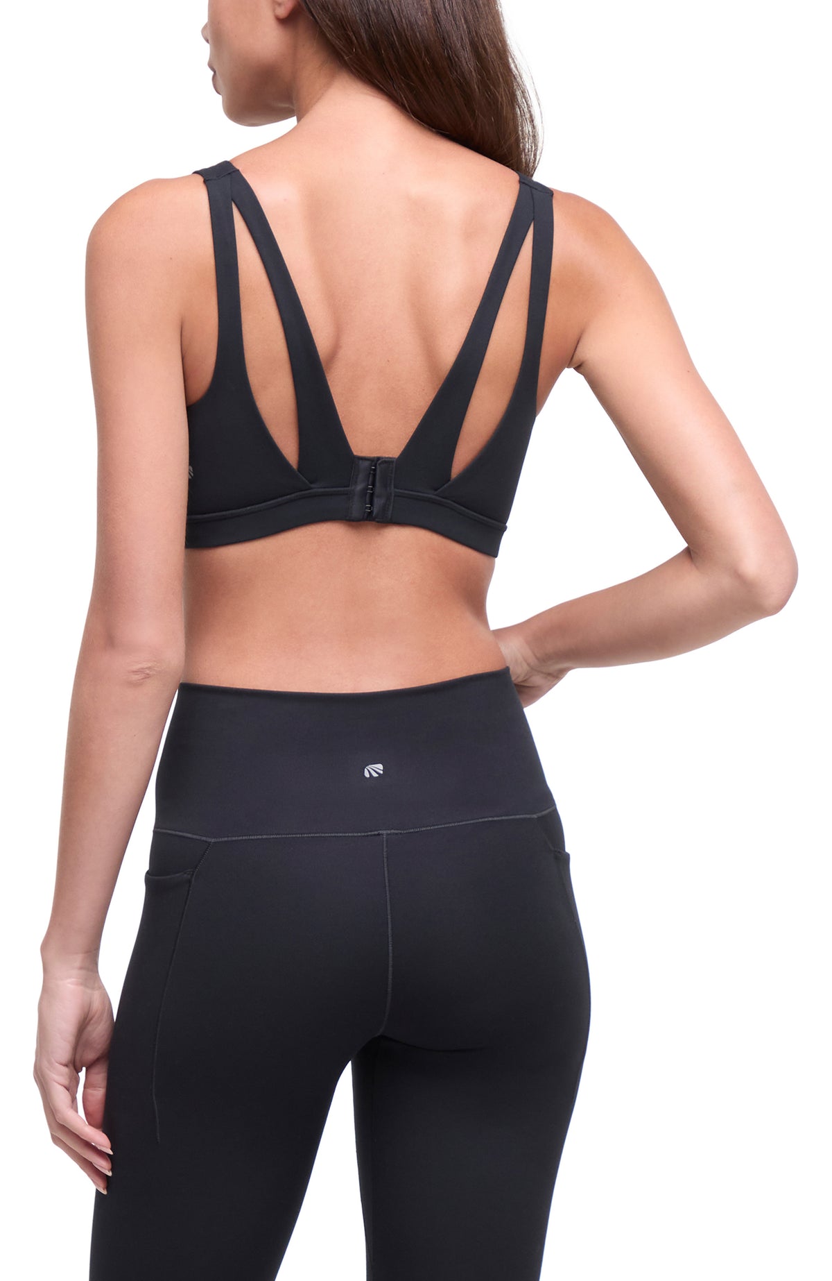 Rear view of a woman wearing a black sports bra with crisscross back straps and black high-waisted leggings against a white background. #color_black