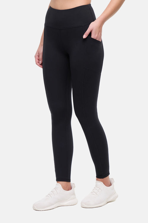 Front view of woman wearing black leggings with hand in side pocket on a white background. #color_black