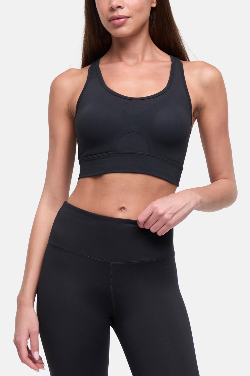 A woman modeling a black sports bra and matching high-waisted leggings against a light gray studio background. #color_black