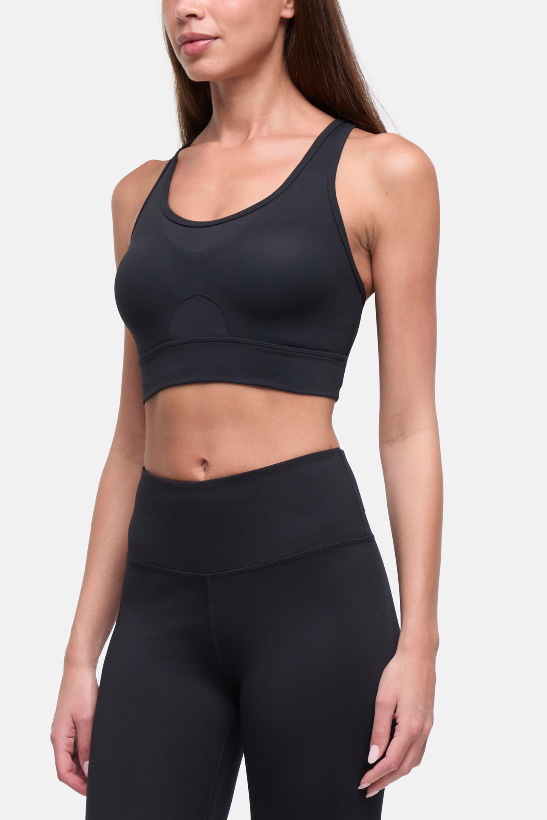 A woman wearing a black athletic sports bra and matching high-waisted leggings against a light gray studio background. #color_black