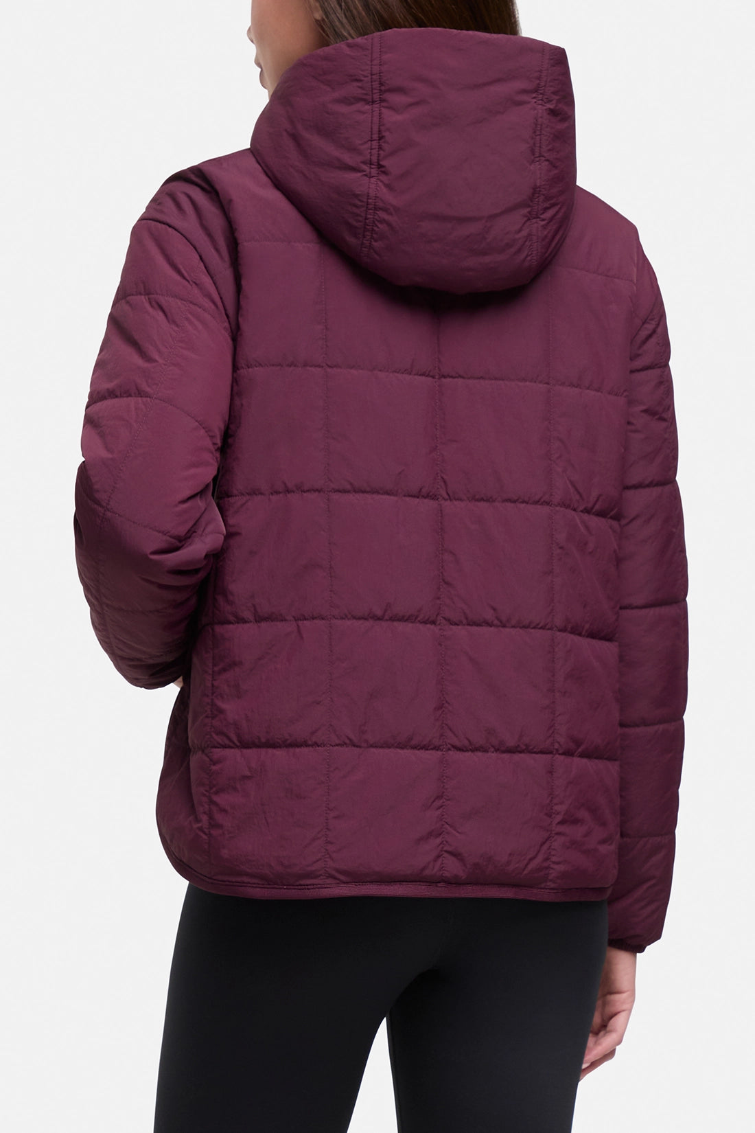 A person shown from the back wearing a quilted puffer jacket in a deep plum or burgundy tone, paired with black leggings, against a plain light gray studio background.