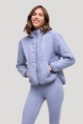 A woman wearing a light periwinkle blue quilted zip-up jacket and matching leggings, posing against a solid light gray background.