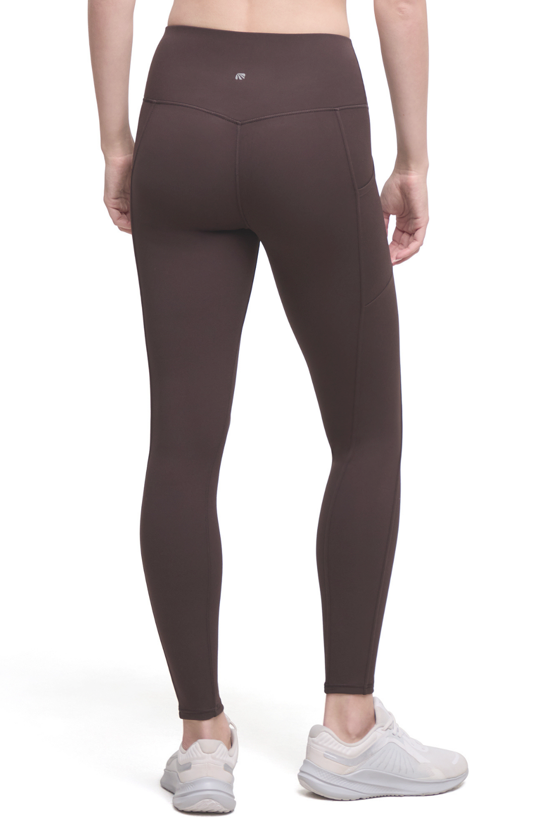 Rear view of a model wearing dark brown high-waisted seamless leggings and white sneakers against a plain white background.
