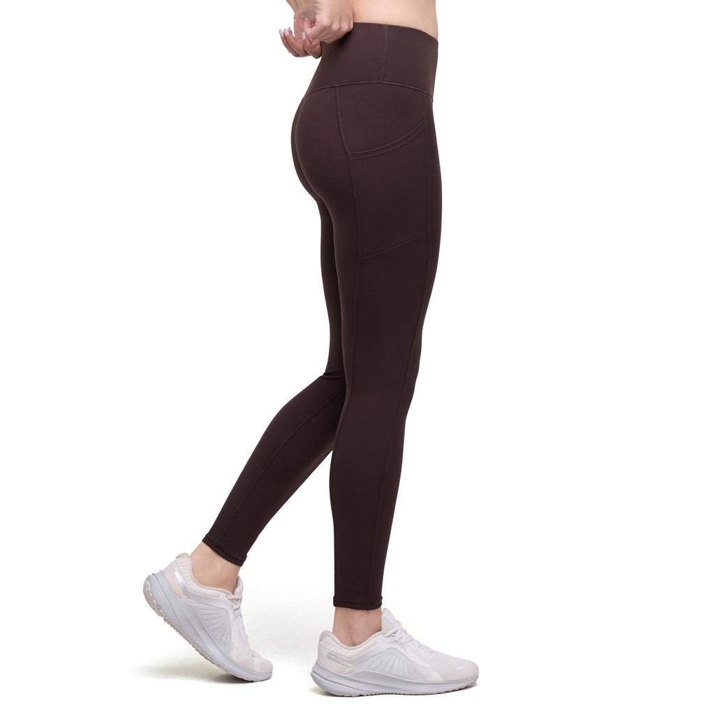 A side profile view of a person wearing dark brown high-waisted leggings and white sneakers against a plain white background.