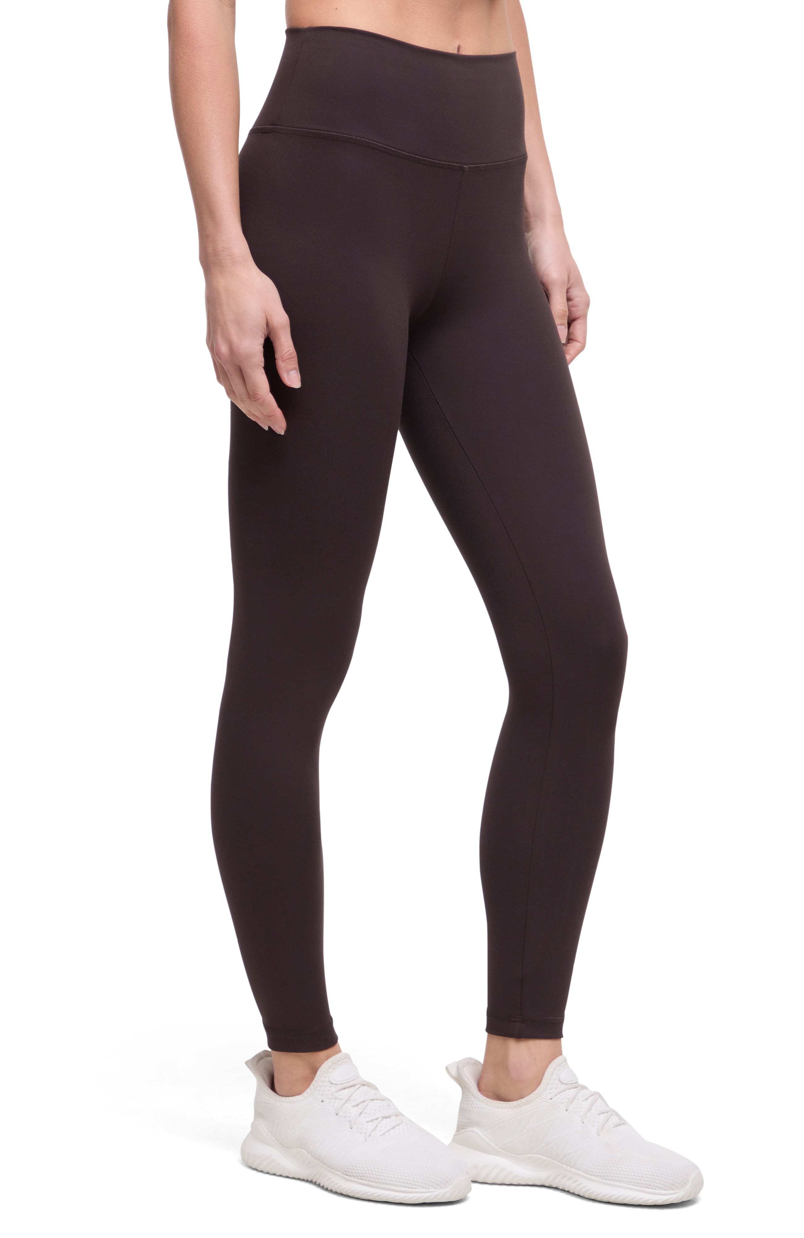 Front view of woman wearing dark brown leggings with a white background. 