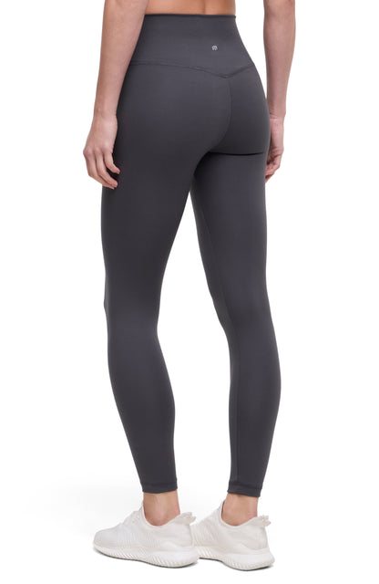 Back view of woman wearing dark gray leggings with a white background. 
