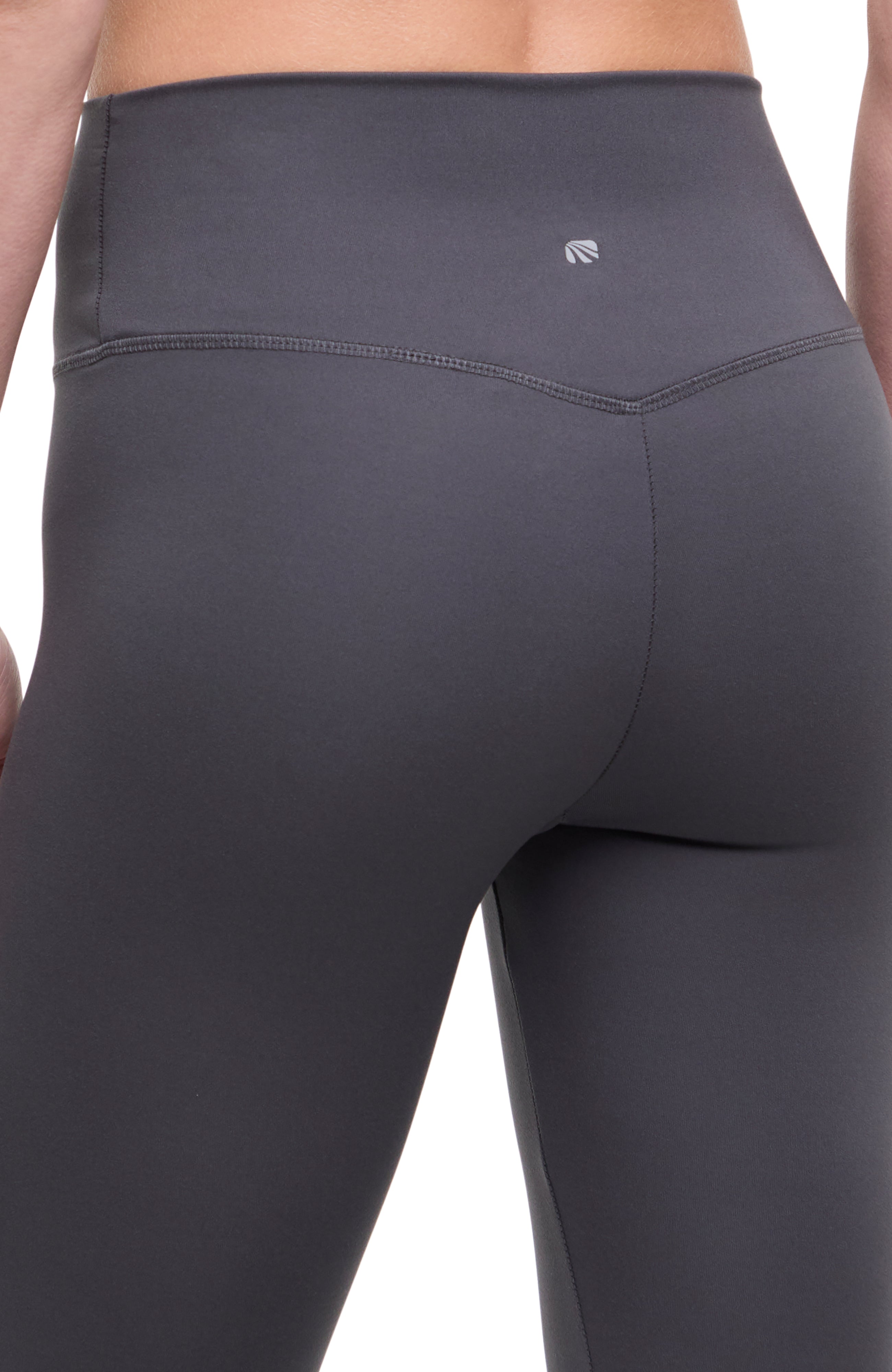 Close up back view of woman wearing dark gray leggings with a white background. 