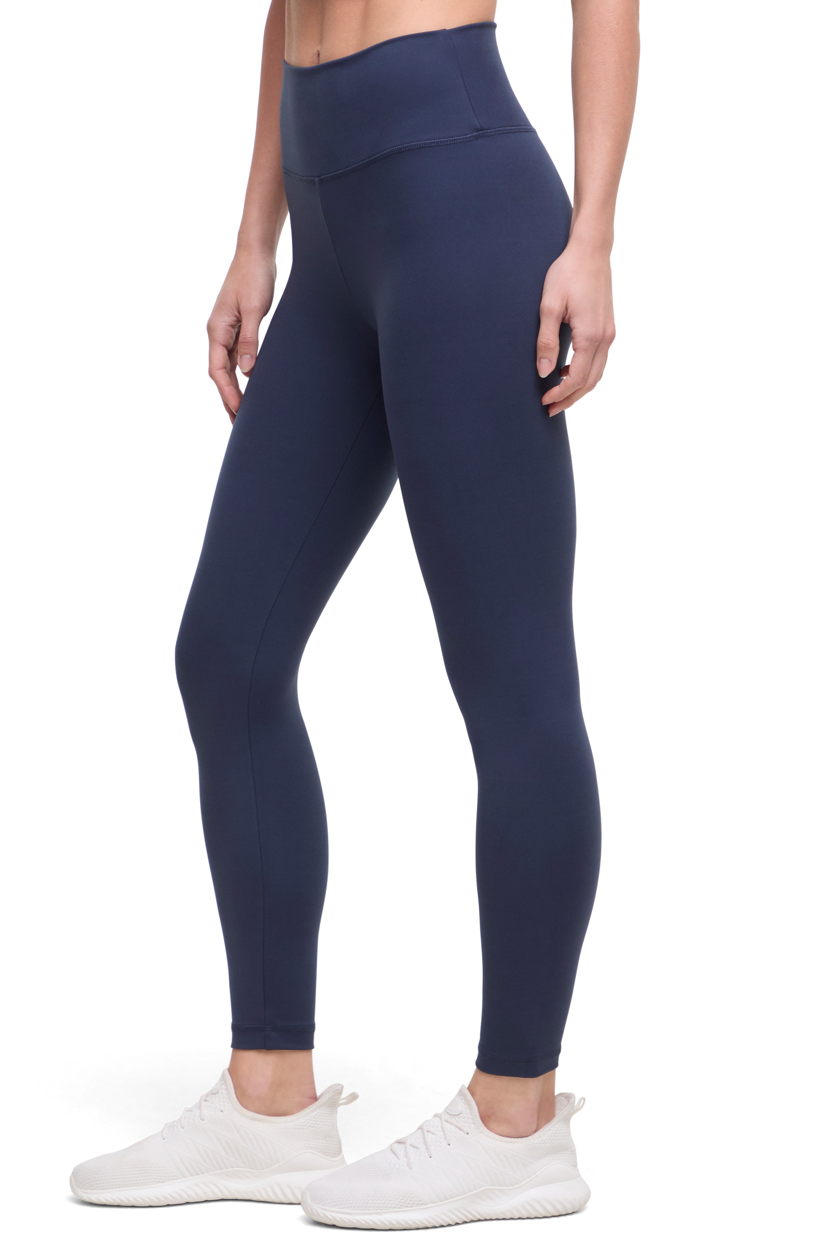 Side view of woman wearing navy leggings with a white background. 