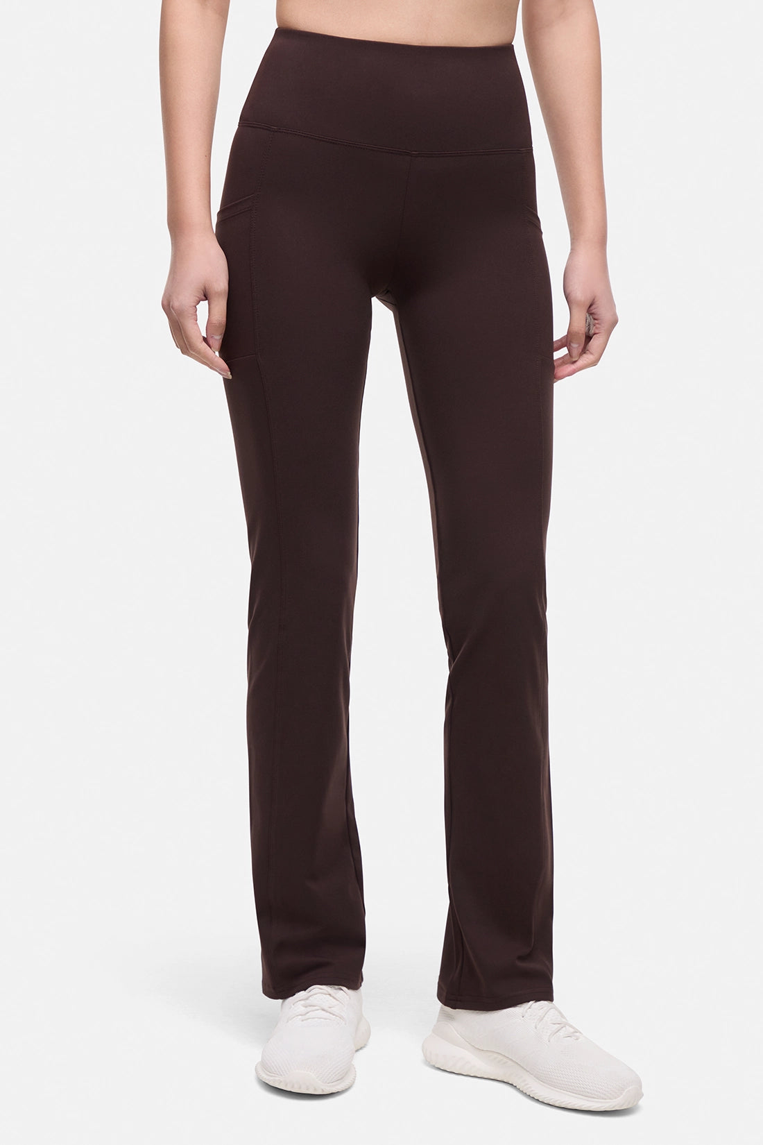 Front view of woman wearing brown yoga pants with a plain background.