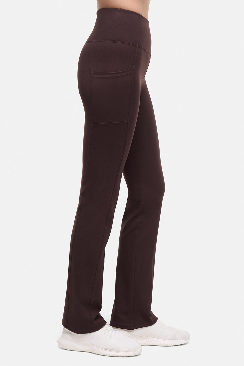 Side view of woman wearing brown yoga pants with a plain background.