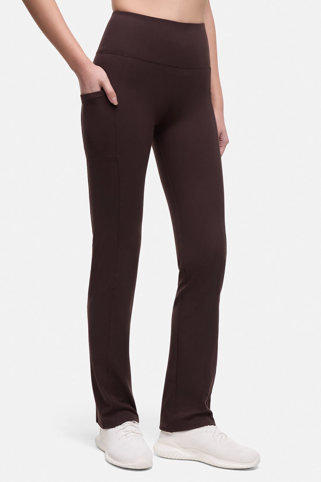 Front view of woman wearing brown yoga pants with a plain background.