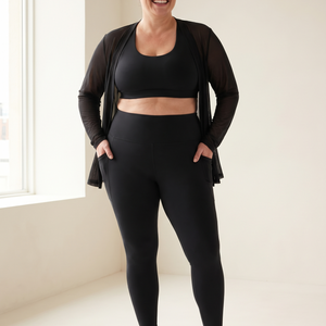 Smiling plus-size woman in black tummy control leggings with pockets and a black sports bra