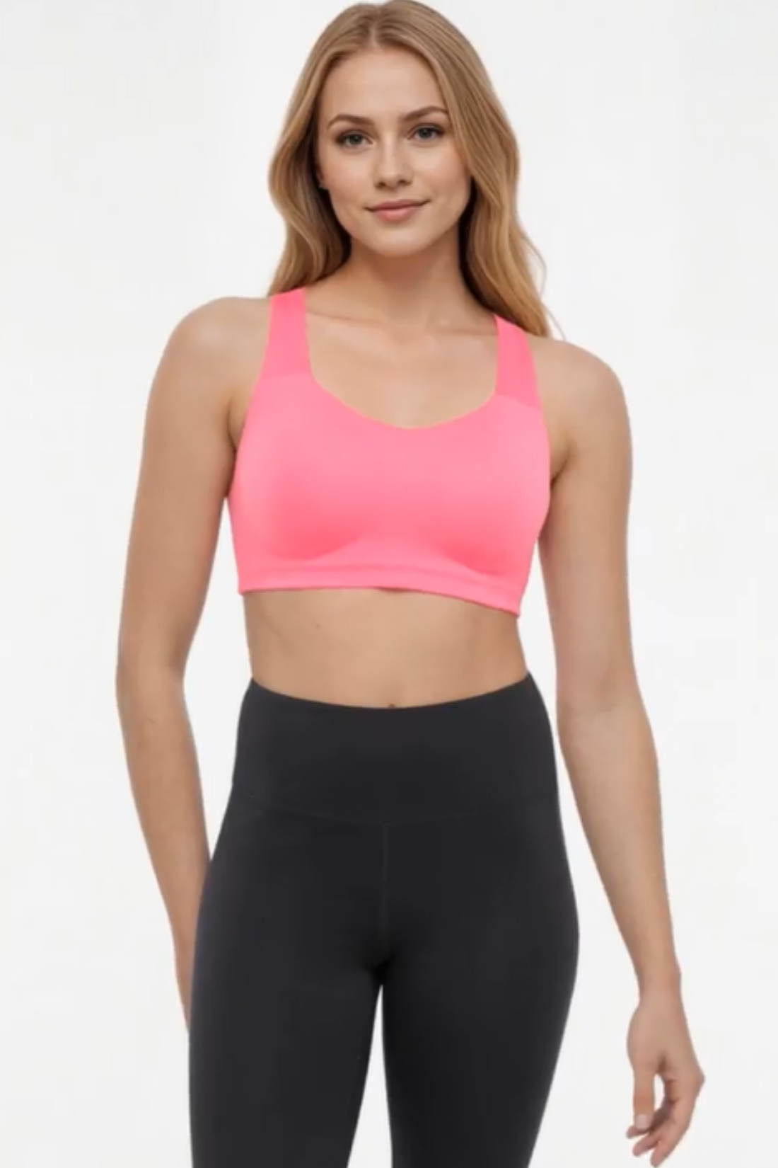 Front view of woman wearing a pink sports bra and black leggings on a white background.