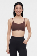 A woman modeling a dark brown scoop-neck sports bra and black high-waisted leggings against a light gray studio background. #color_french-roast