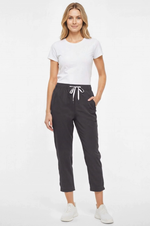 A woman modeling a white short-sleeve crewneck t-shirt and dark charcoal gray cropped jogger pants with a white drawstring, paired with white sneakers, against a plain white studio background. #color_phantom
