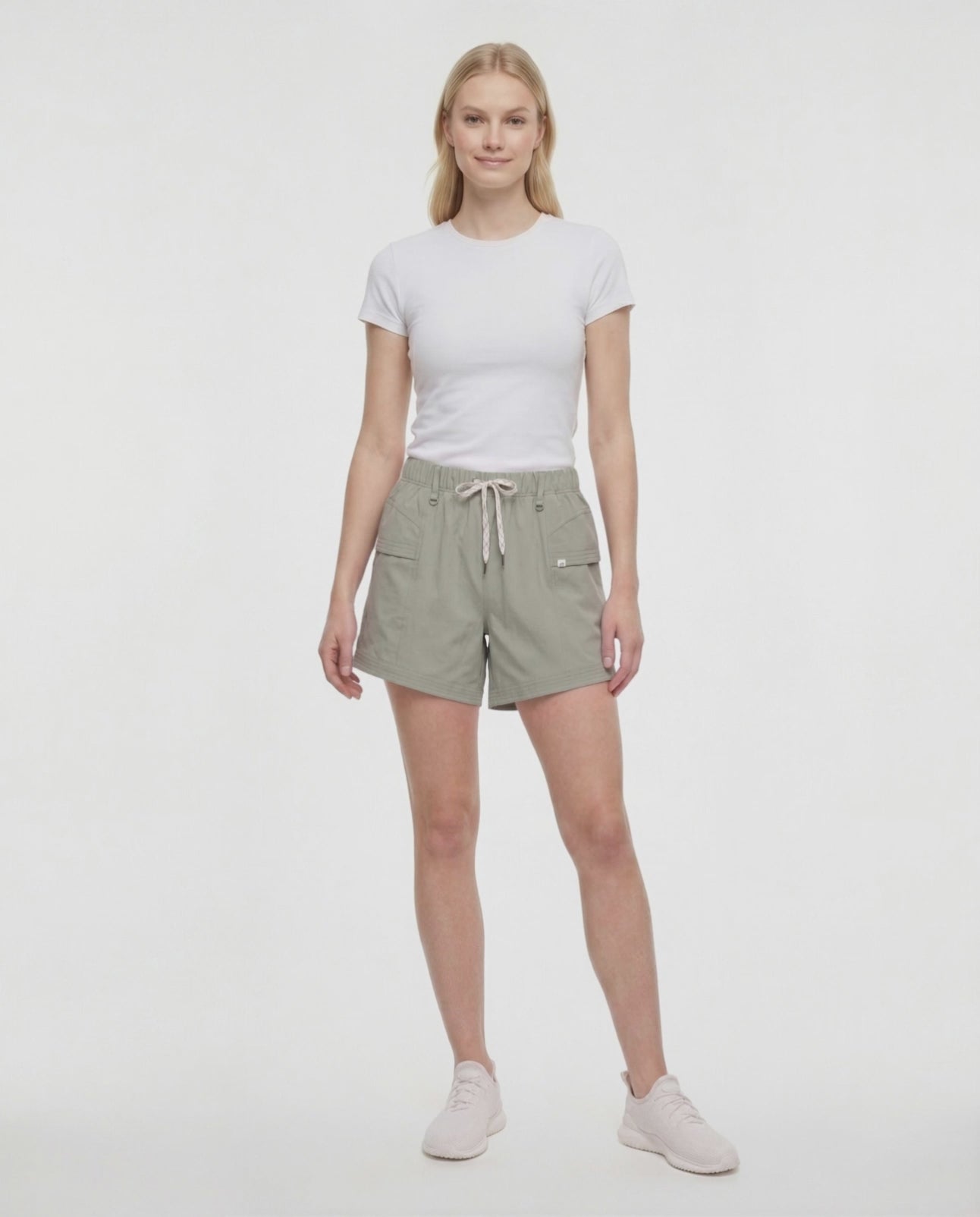 Video view of woman wearing sage green shorts with white drawstring waist, white top and white sneakers on a white background. 