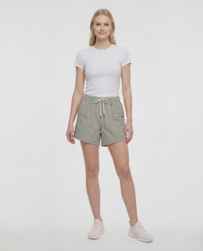 Video view of woman wearing sage green shorts with white drawstring waist, white top and white sneakers on a white background. 