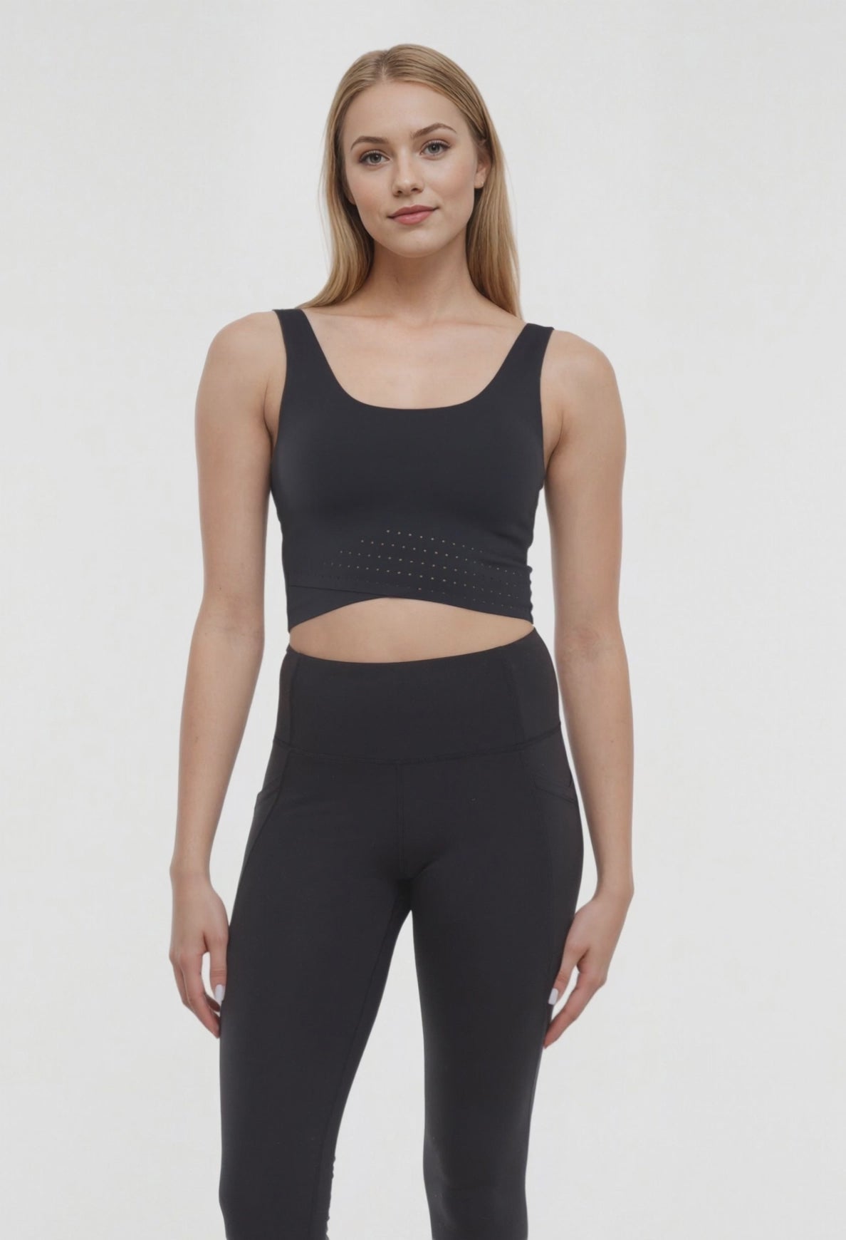 Video view of woman wearing a black sports bra and black leggings on a white background. 