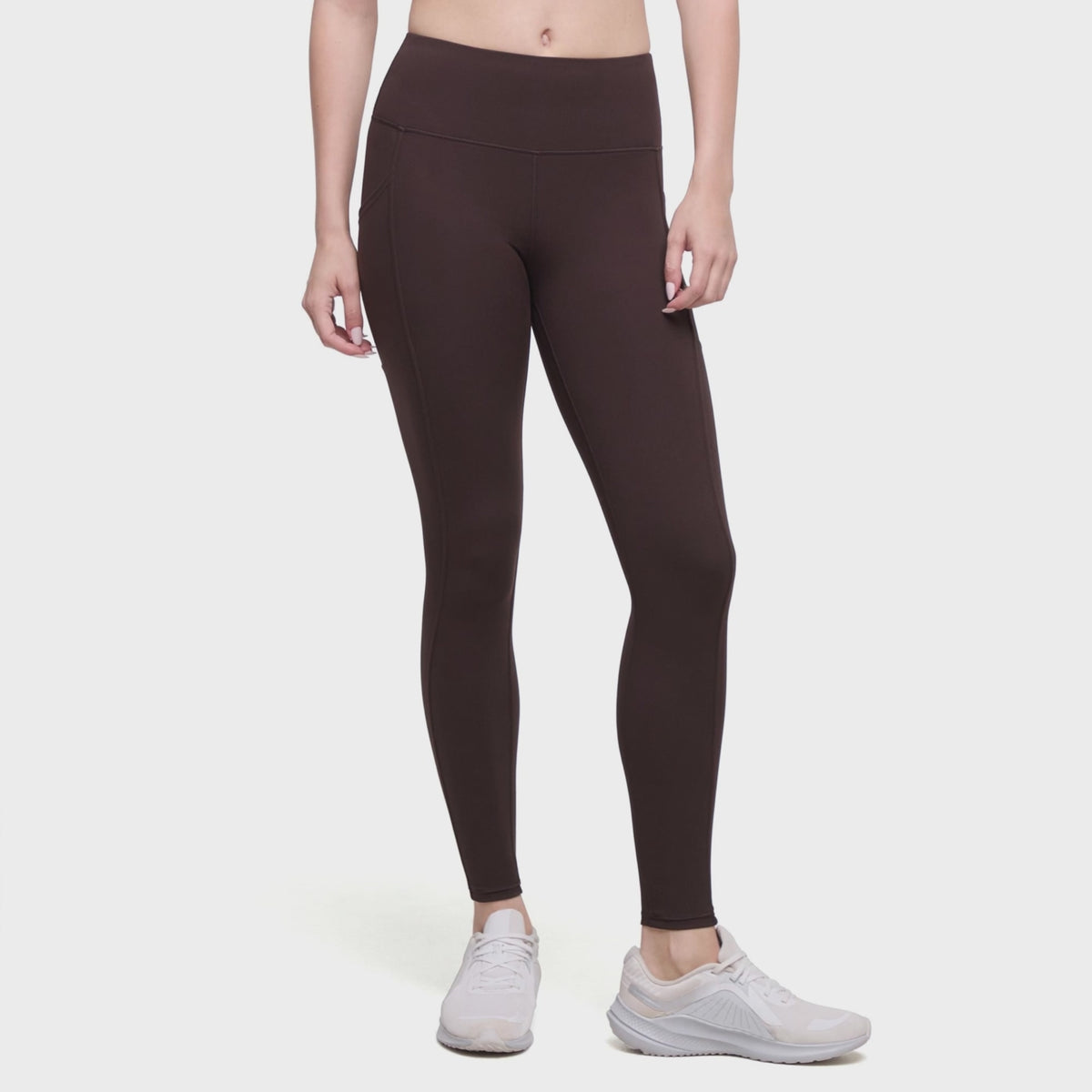 Video of A model wearing dark brown high-waisted leggings and white sneakers, shown from the waist down against a plain white background.