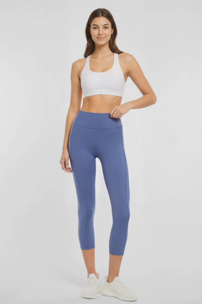 Video view of woman wearing blue capris and white sneakers on a light gray background.. 