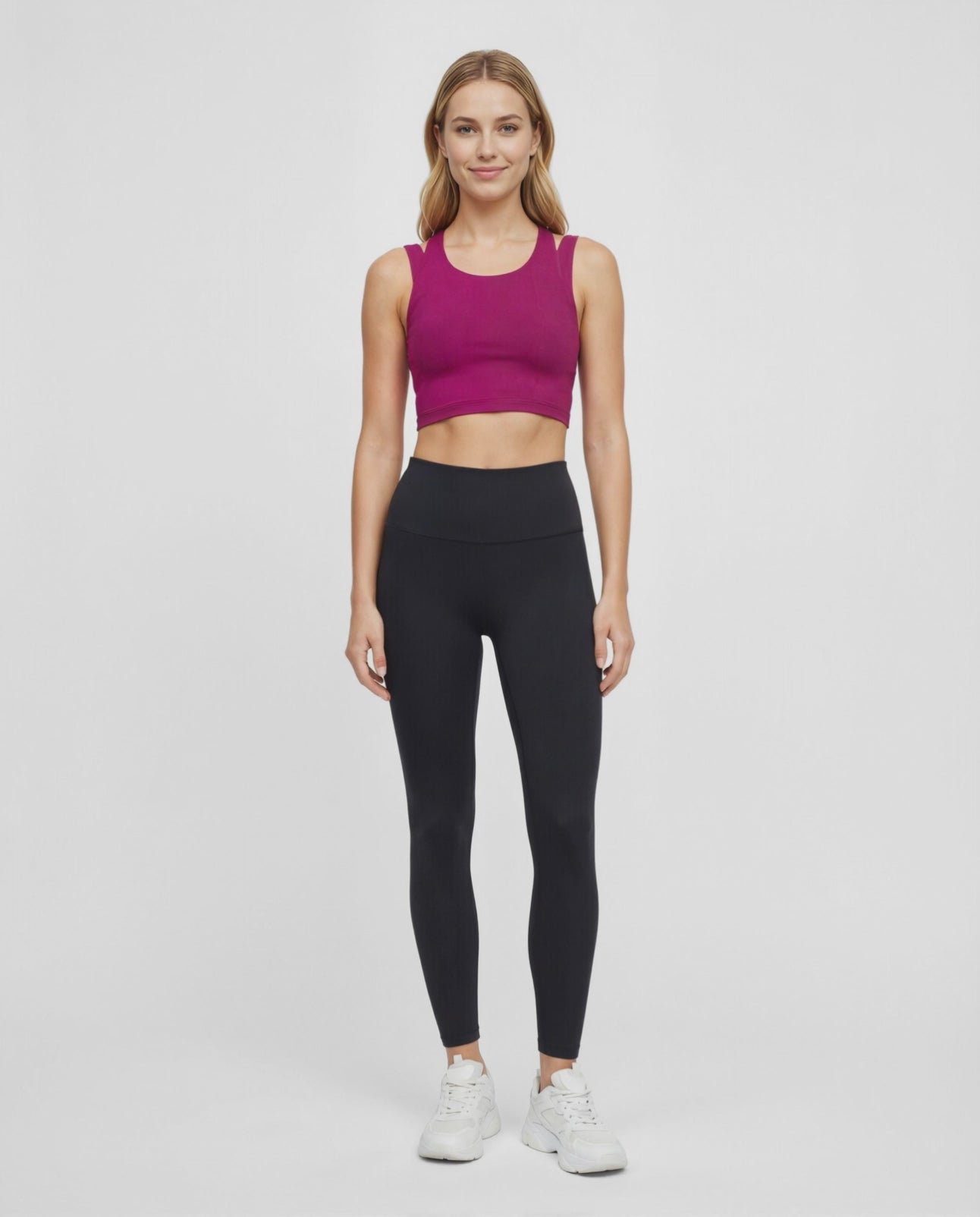 Video view of woman wearing a bright burgundy sports bra and black leggings on a white background. #color_magenta-purple