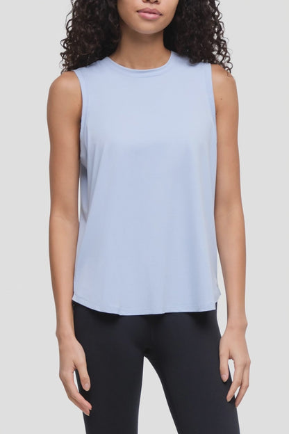 Video of a woman wearing a light blue sleeveless crewneck tank top and black leggings, shown from the waist up against a plain light gray studio background. 