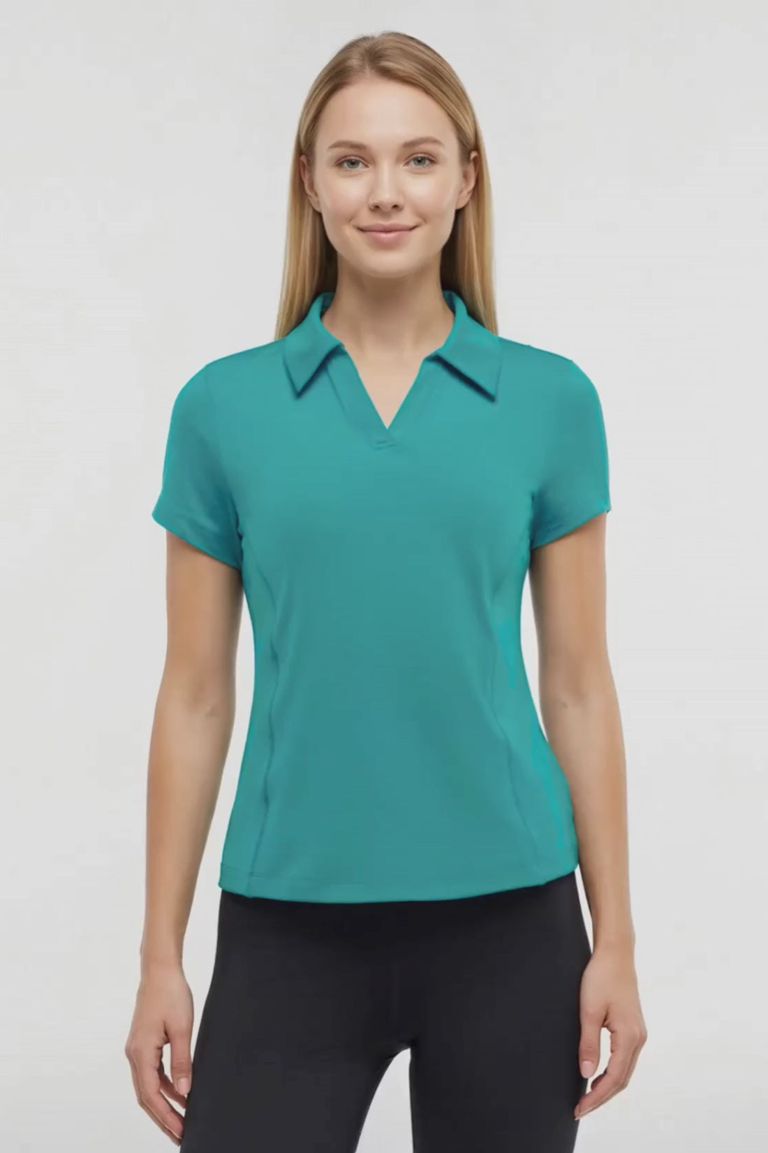 Video view of woman wearing a teal polo shirt and black pants on a white background. #color_quetzal-green