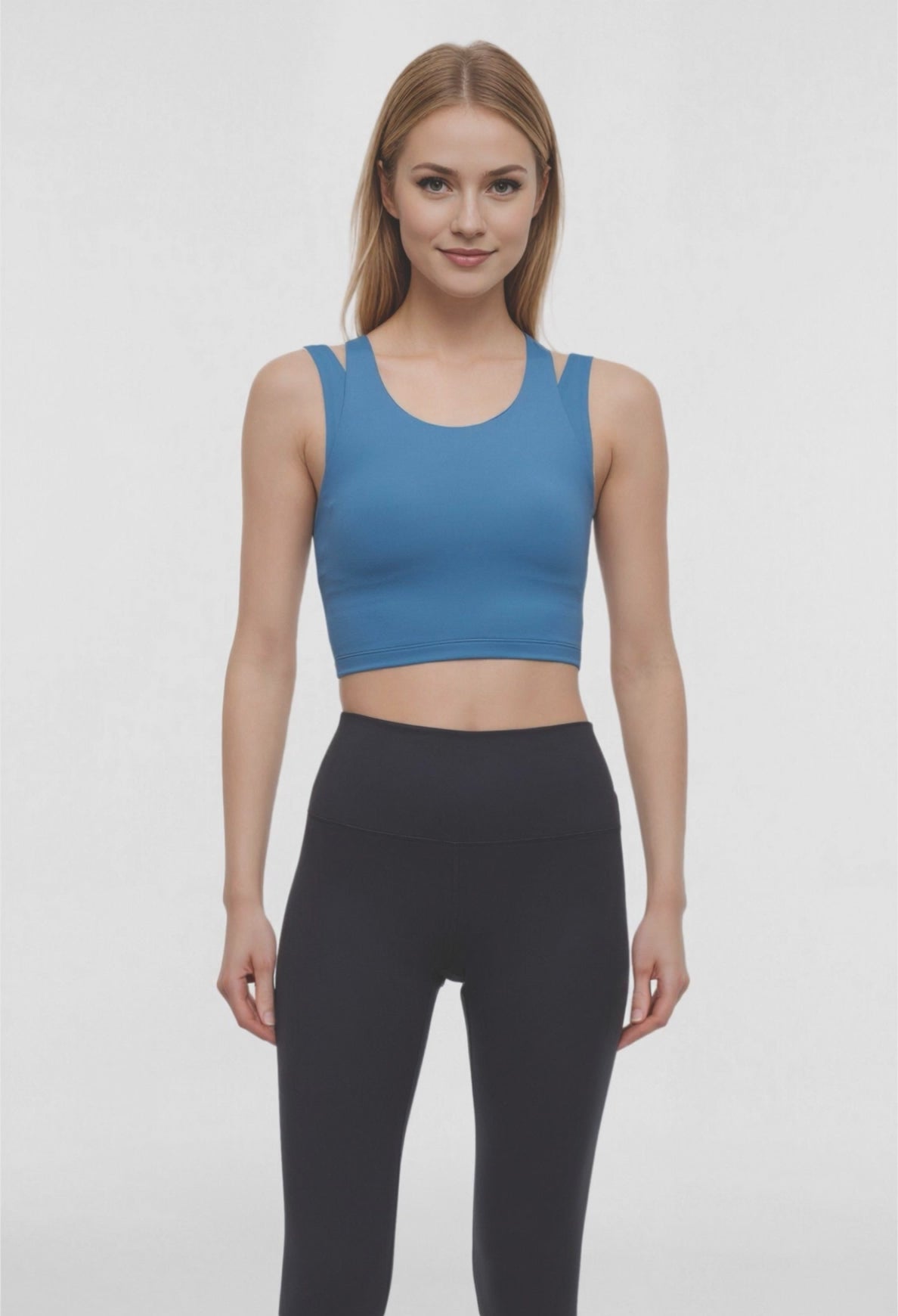 Video view of woman wearing a blue sports bra and black leggings on a white background. 