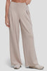 Video of A model wearing high-waisted, wide-leg pleated trousers in a light taupe-beige color with front pleat detail, paired with light-colored sneakers, against a plain light gray studio background. #color_atmosphere