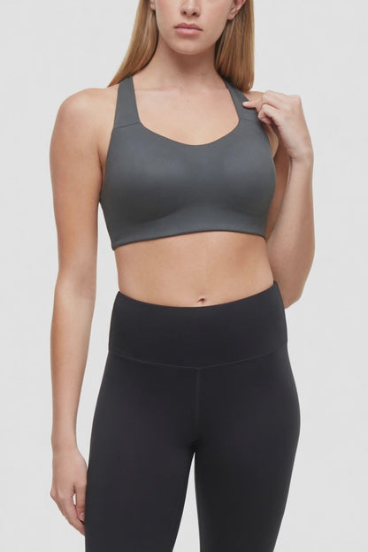 Video view of woman wearing a gray sports bra with strappy back and black leggings on a white background. 