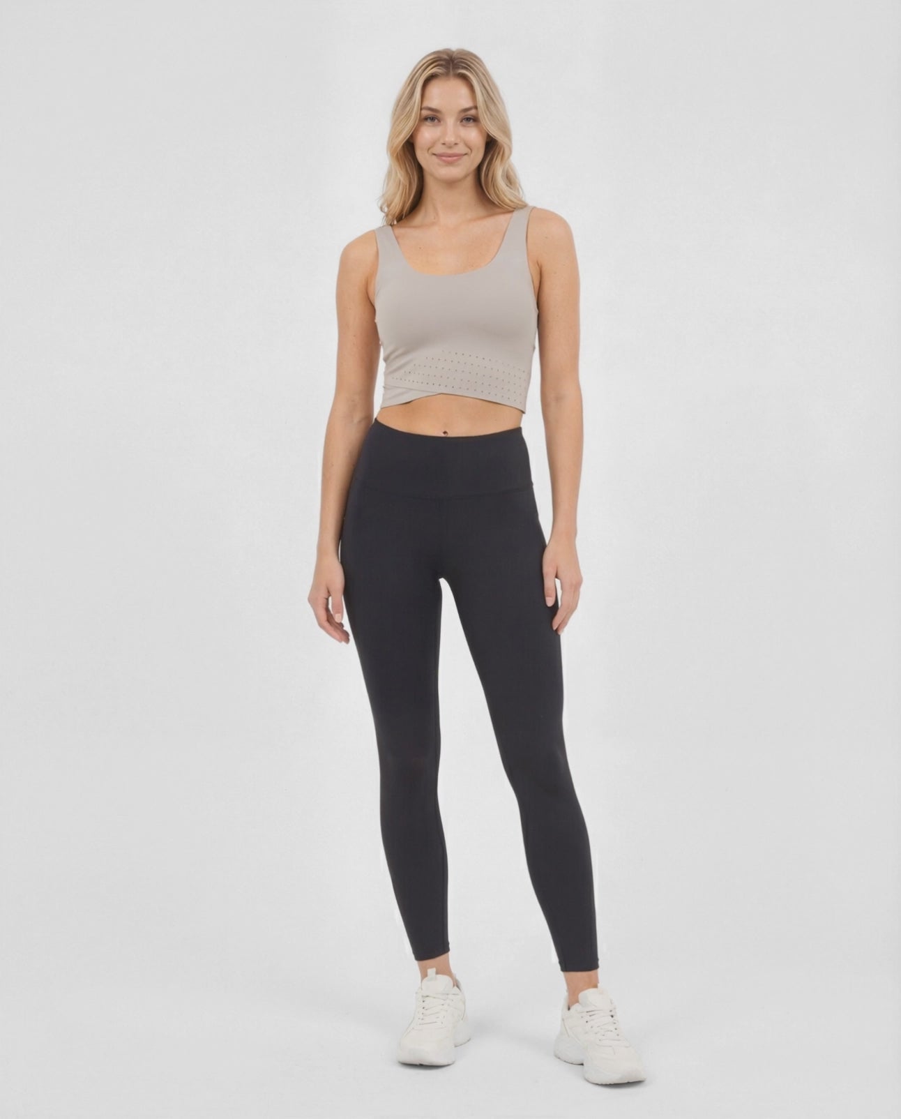 Video view of woman wearing a beige sports bra and black leggings on a white background. 