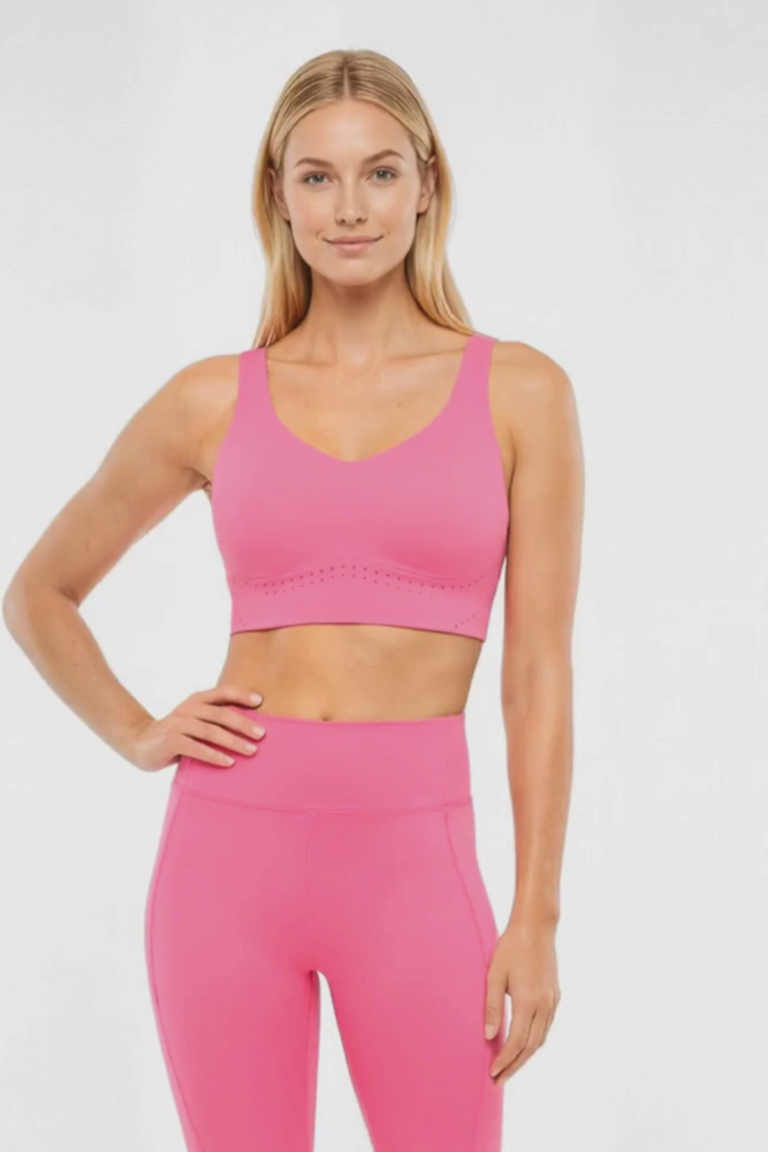 Video view of woman wearing a pink sports bra and matching pink leggings on a white background.  #color_pink-flambe