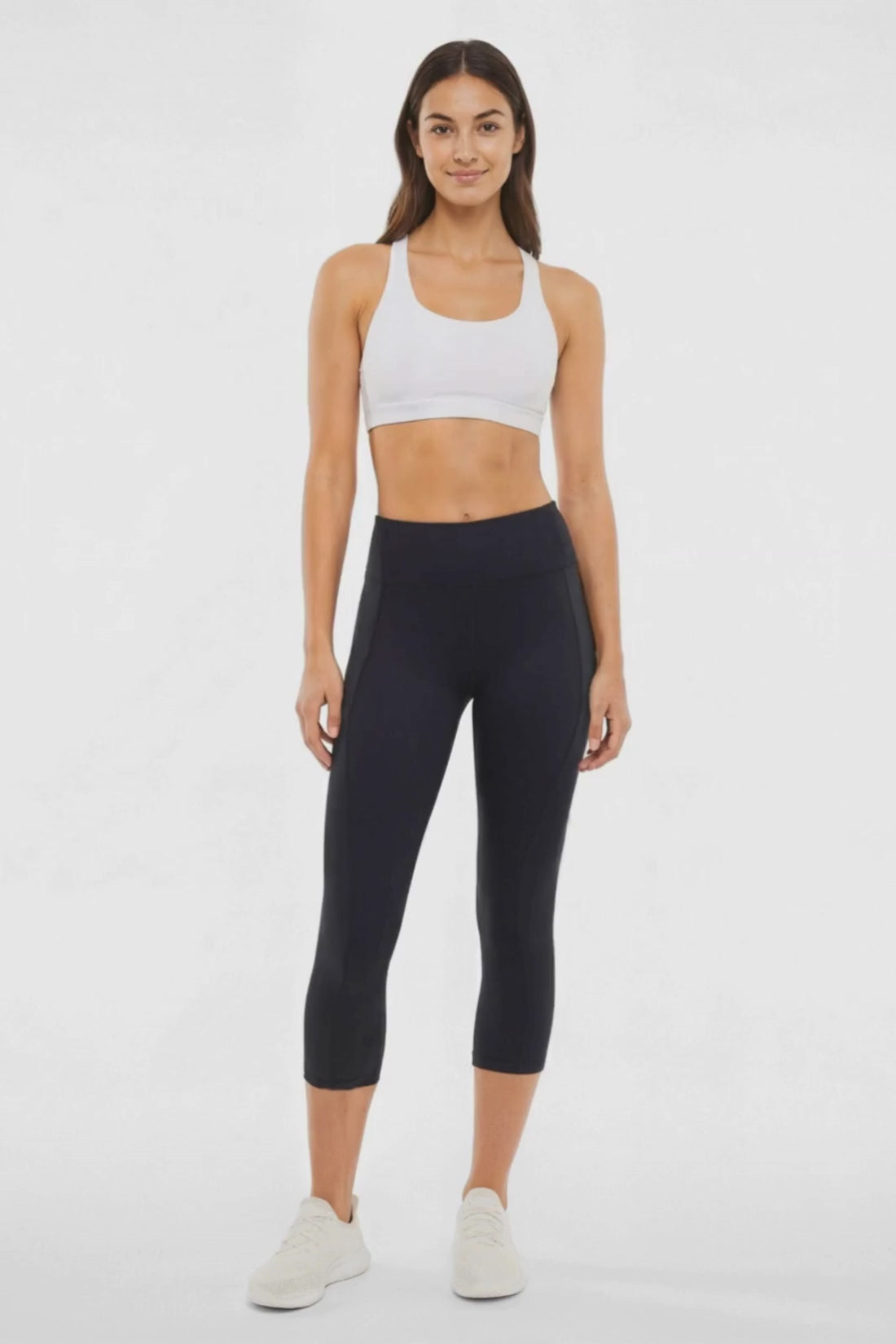 Video view of woman wearing black capris and white sneakers on a light gray background. #color_black