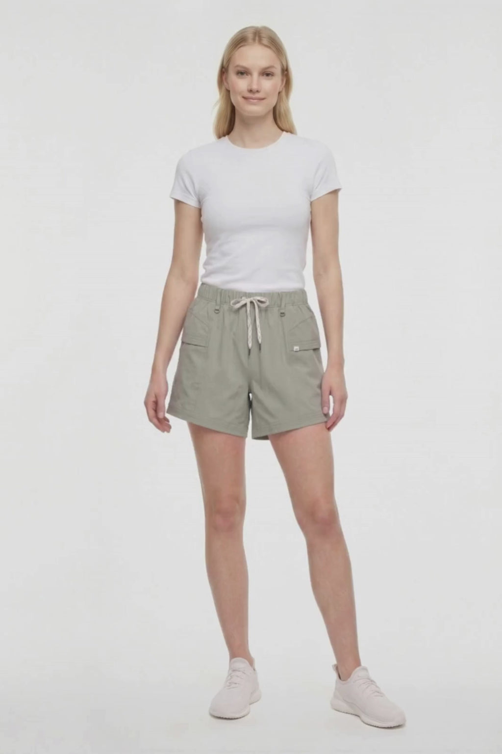 Video view of woman wearing sage green shorts with white drawstring waist and white sneakers on a white background. #color_shadow